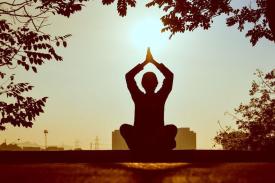 Person in nature sitting with their legs crossed, arms up above their head with palms touching each other Person in nature sitting with their legs crossed, arms up above their head with palms touching each other